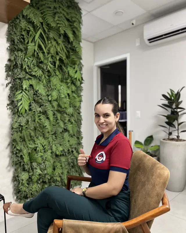 Colaboradora sorrindo na recepção do escritório, ao lado de uma parede verde.